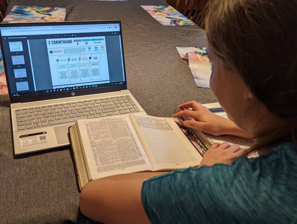 Girl looking at a computer screen with her Bible open.